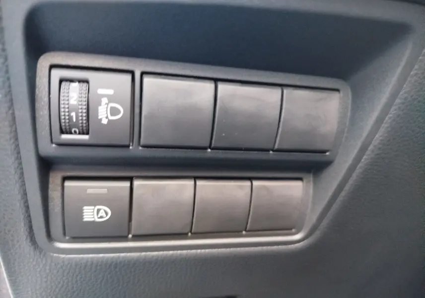 Gros plan sur les commandes noires de réglage des phares et de l’éclairage automatique dans une Toyota Yaris blanche.