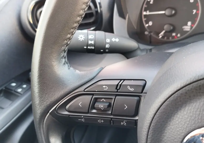 Gros plan sur les commandes au volant noir de la Toyota Yaris 2023, avec tableau de bord et commodo en arrière-plan.