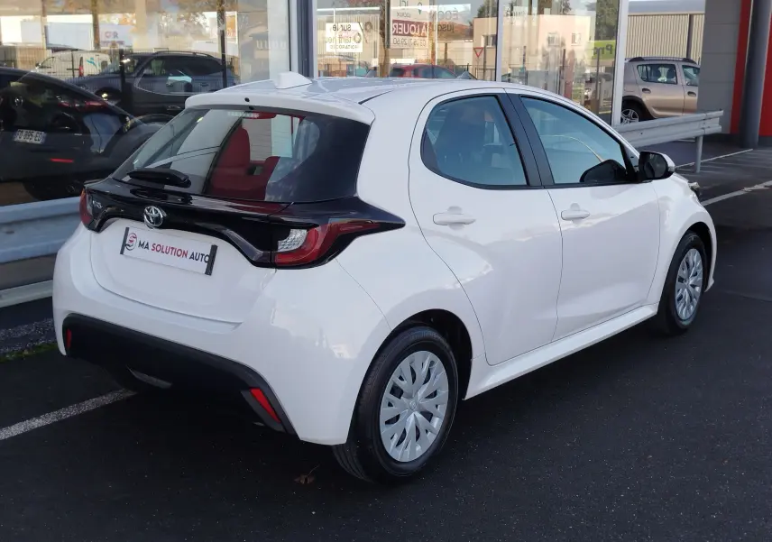 Vue 3/4 arrière droite d'une Toyota Yaris blanche pure 2023 avec toit noir et feux arrière distinctifs.