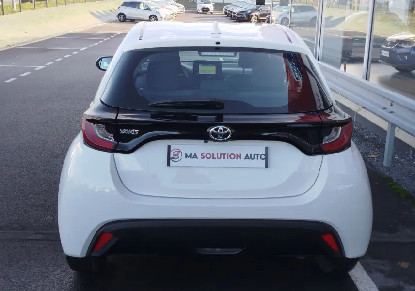 Vue arrière d'une Toyota Yaris blanche avec toit noir, mettant en valeur le logo Toyota et les feux arrière distinctifs.
