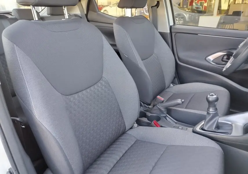 Vue intérieure côté avant droit de la Toyota Yaris blanche, montrant les sièges en tissu gris et le levier de vitesses manuel.