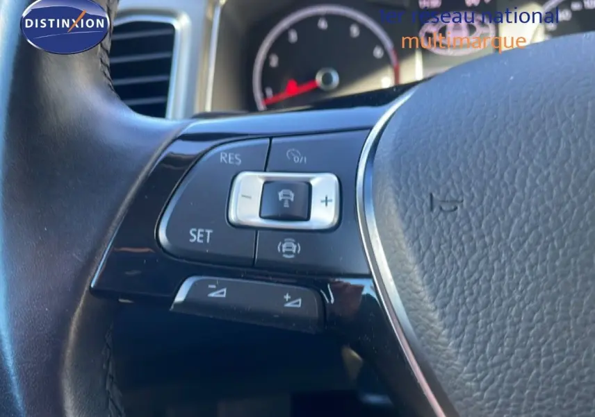 Gros plan sur les commandes de régulateur de vitesse au volant cuir noir du Volkswagen T-Roc 1.5 TSI bleu Ravenna.