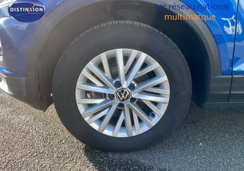 Gros plan sur la roue avant gauche d'un Volkswagen T-Roc bleu Ravenna métallisé, avec jante alliage argentée.