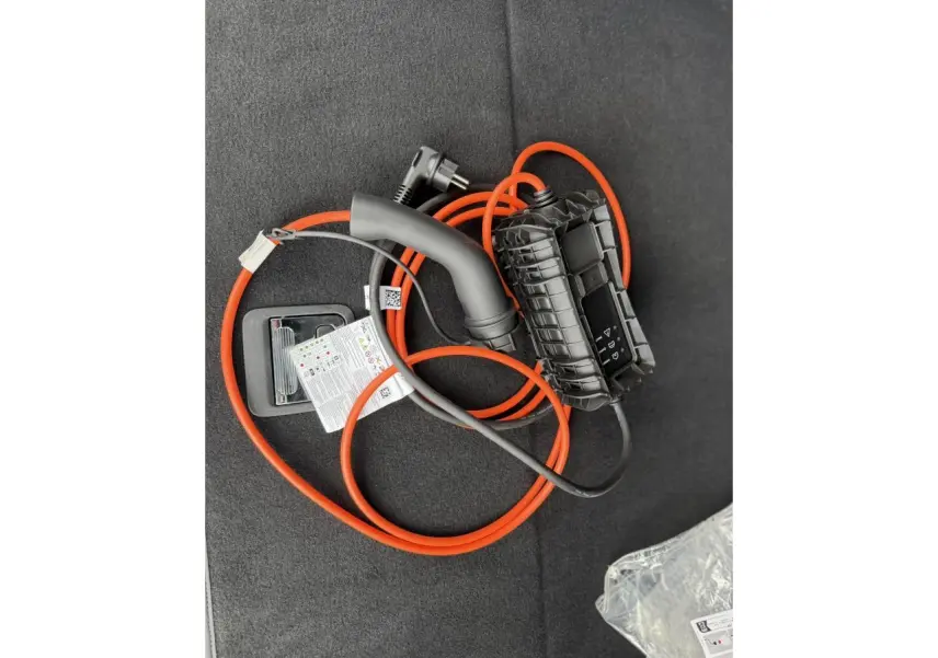 Câble de recharge orange posé dans le coffre d’un Peugeot 3008 Plug-in Hybrid noir Perla, vue intérieure.