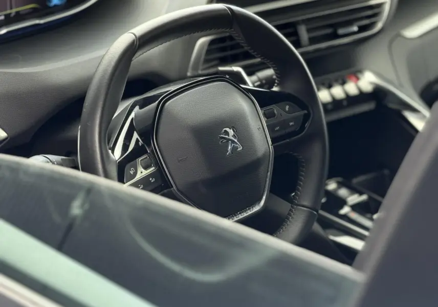 Vue rapprochée du volant noir cuir du Peugeot 3008 2024 avec commandes intégrées et tableau de bord sombre.