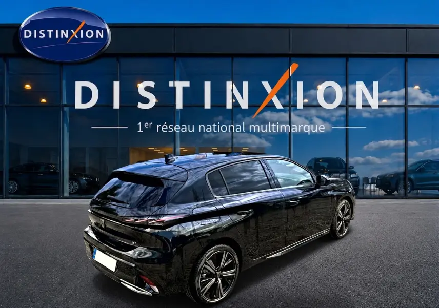 Vue 3/4 arrière droite d'une Peugeot 308 noire 2025 garée devant une vitrine Distinxion, jantes alliage visibles.