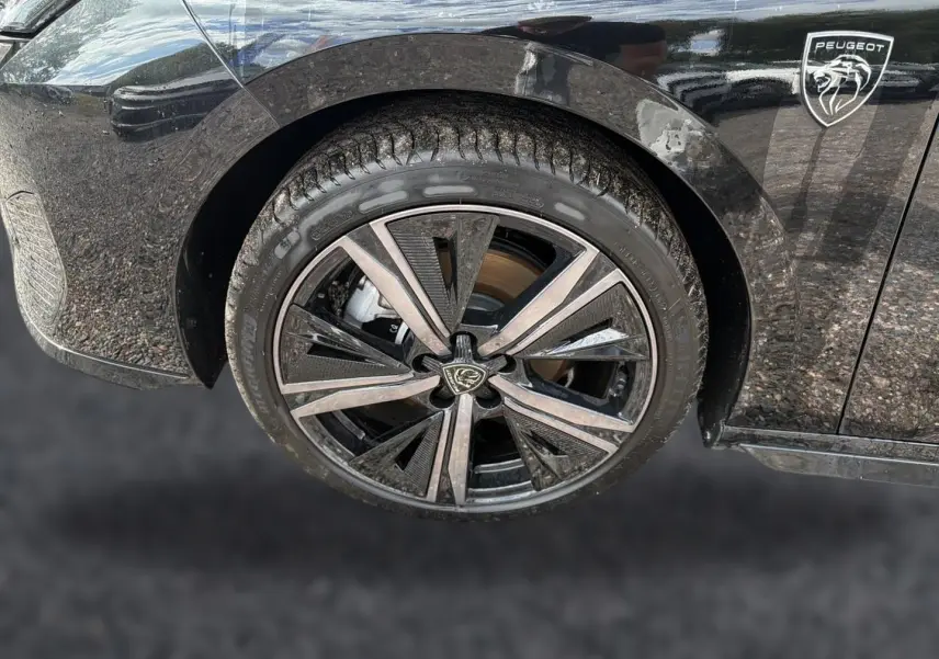 Gros plan sur la roue avant gauche noire d’une Peugeot 308 1.2 hybrid 145 GT avec jante alu au design moderne.