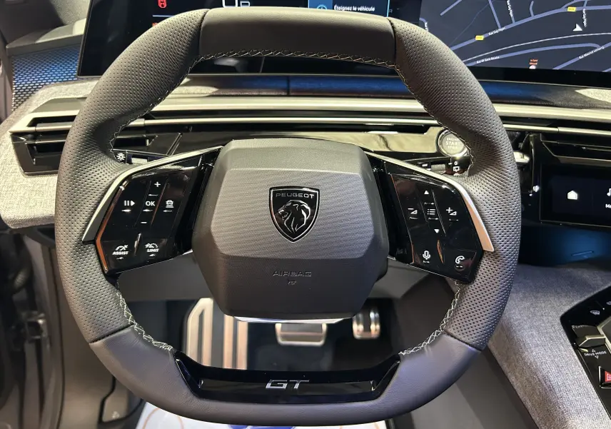 Gros plan sur le volant GT perforé et multifonction du Peugeot 5008 III Hybrid avec tableau de bord numérique.