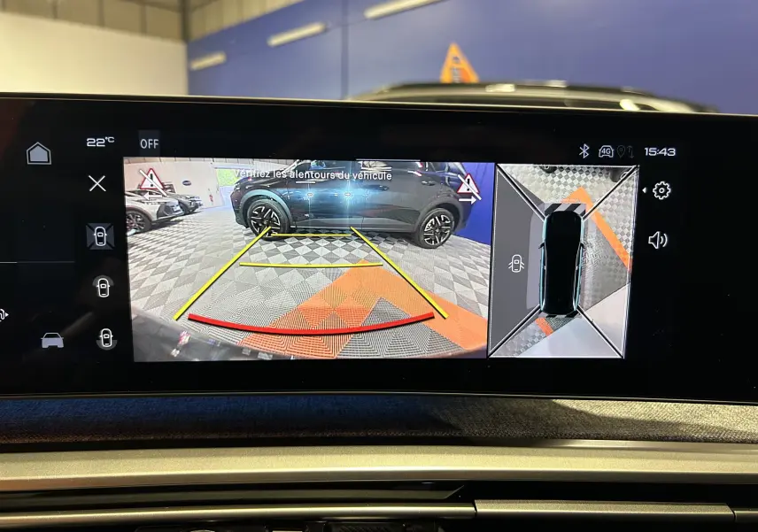 Écran multimédia montrant la caméra de recul et la vue 360° d'un Peugeot 5008 gris Artense en stationnement intérieur.