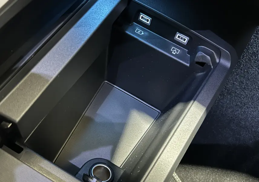 Gros plan sur la console centrale noire du Peugeot 5008 III GT Hybrid avec ports USB et prise 12V.