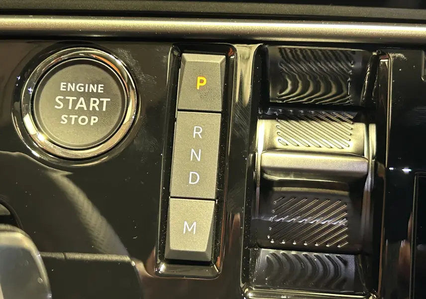 Gros plan sur la console centrale noire brillante du Peugeot 5008 III GT Hybrid avec bouton start/stop et commandes de boîte automatique.