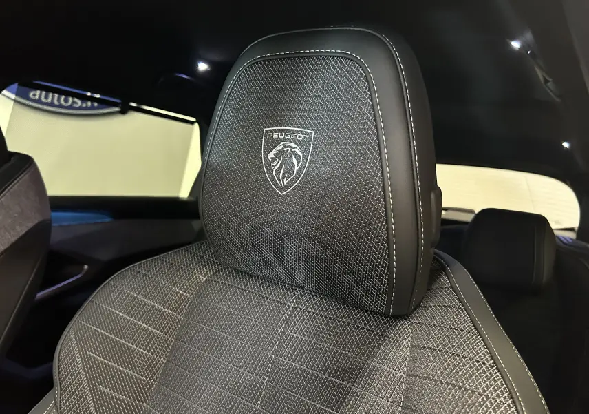 Gros plan sur l'appui-tête avant avec logo Peugeot brodé, intérieur sombre du SUV 5008 hybride 2025.