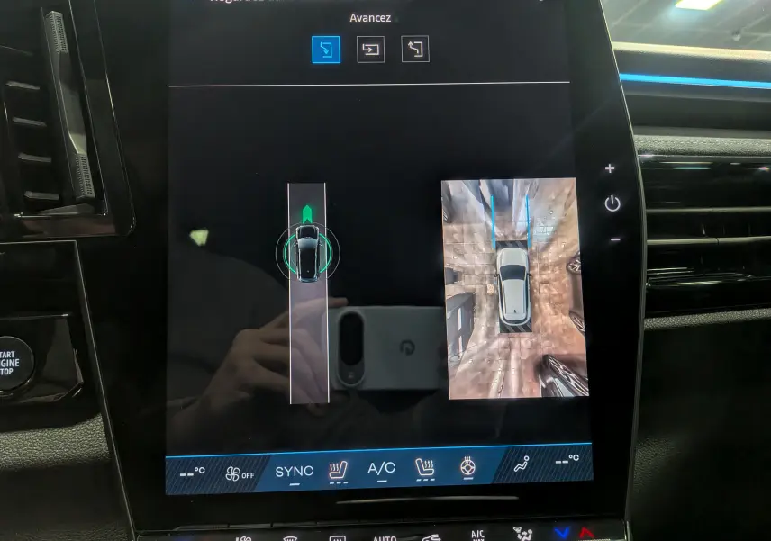 Écran tactile du tableau de bord du Renault Austral 2025 montrant la vue 360° et la trajectoire de stationnement en blanc nacré satin.