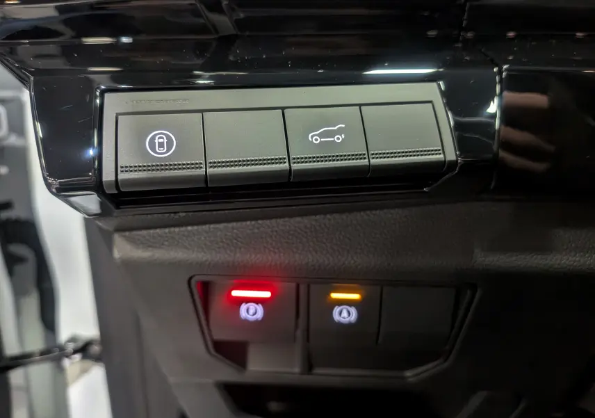 Gros plan sur les boutons de commande du tableau de bord du Renault Austral blanc nacré satin, avec éclairages rouge et orange.