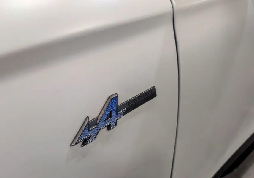 Gros plan sur l'emblème Esprit Alpine bleu sur la porte blanche nacrée satinée du Renault Austral 2025.