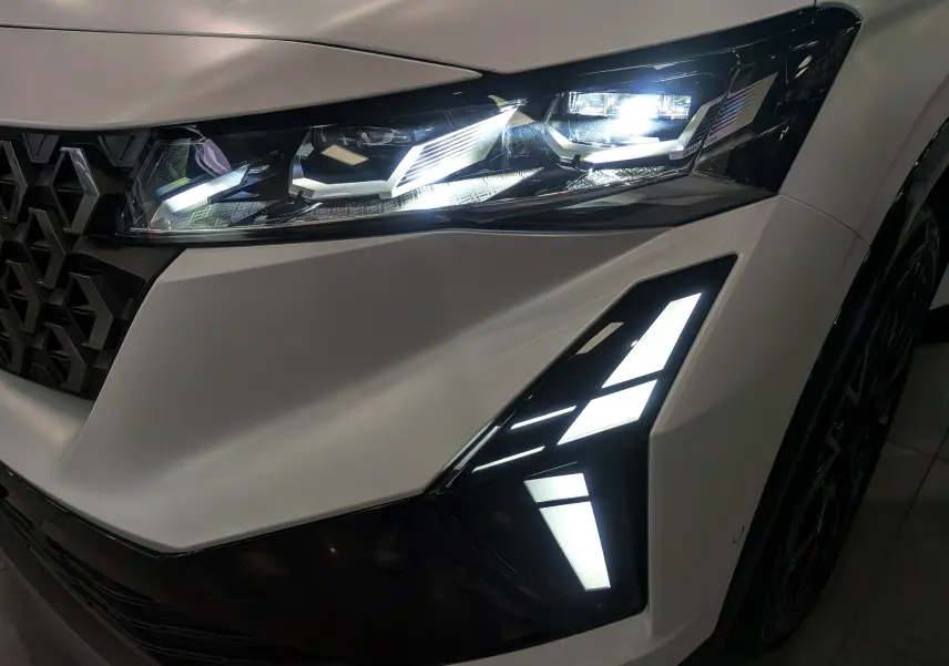 Gros plan sur le phare avant droit allumé du Renault Austral blanc nacré satin avec calandre noire et feux LED distinctifs.