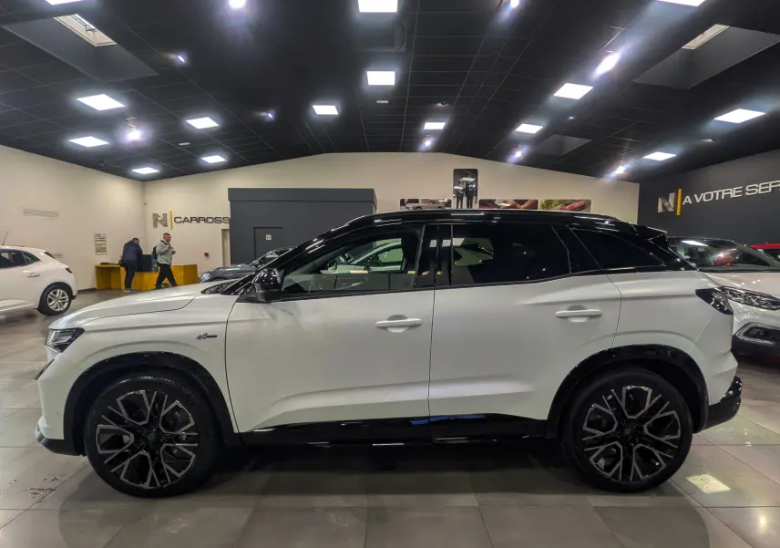 Profil latéral droit du Renault Austral blanc nacré avec toit noir et jantes noires au design distinctif en showroom.