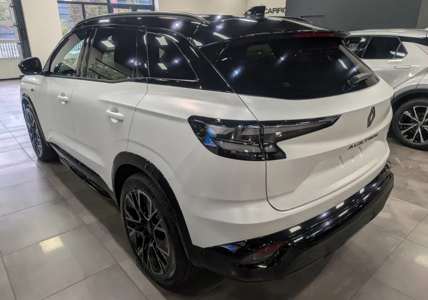 Vue 3/4 arrière droite du Renault Austral blanc nacré avec toit noir et jantes noires en intérieur showroom.