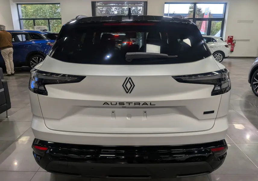Vue arrière du Renault Austral blanc nacré satin avec toit noir, soulignant ses feux arrière fins et son logo central.