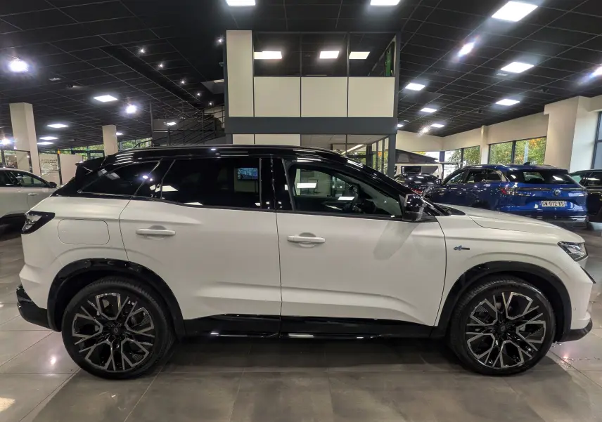 Profil côté gauche du Renault Austral blanc nacré satin avec toit noir et jantes noires en concession.