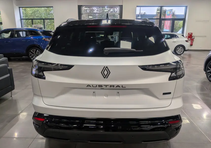 Vue arrière d'un Renault Austral blanc nacré satin avec toit noir, mettant en valeur son logo et ses feux arrière fins.