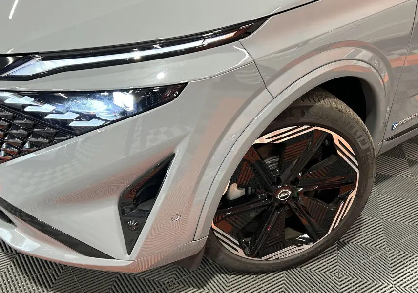 Gros plan sur l'avant droit du Nissan Qashqai gris céramique, mettant en valeur le phare LED et la jante noire à motifs blancs.