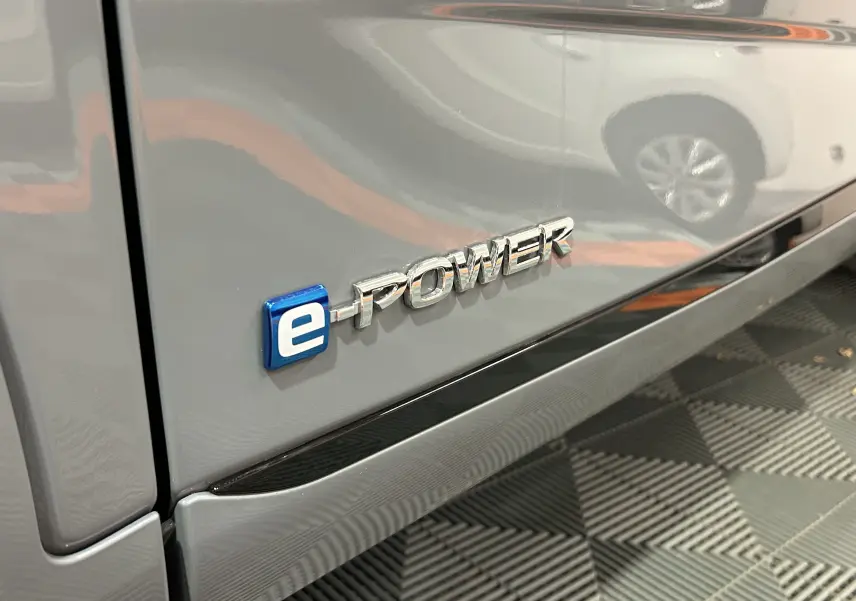 Gros plan sur l’inscription e-POWER côté gauche d’un Nissan Qashqai gris céramique métal avec reflet d’un autre véhicule.