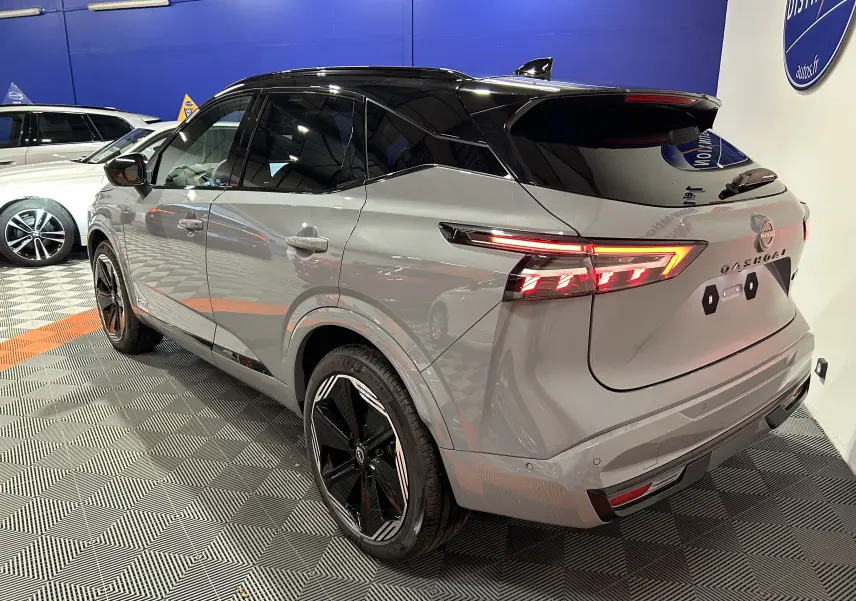 Vue 3/4 arrière droite du Nissan Qashqai gris céramique métallisé avec toit noir panoramique et feux LED allumés.