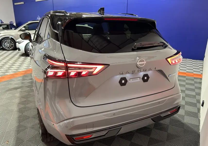 Vue 3/4 arrière droite du Nissan Qashqai gris céramique métal avec feux LED allumés et toit noir brillant.