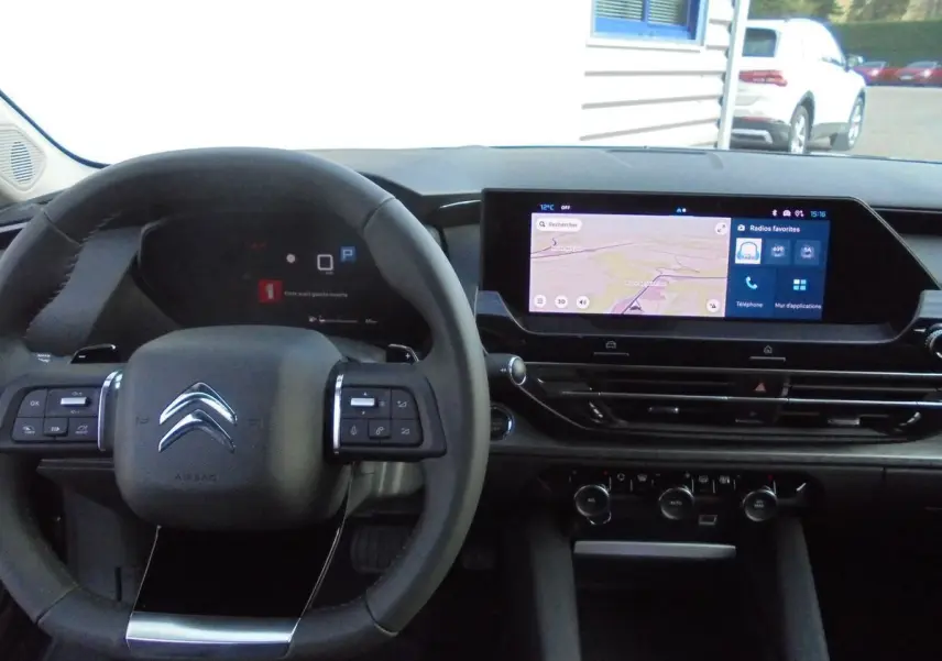 Vue intérieure du poste de conduite du Citroën C5 X gris platinum, avec volant multifonction et écran tactile central allumé.