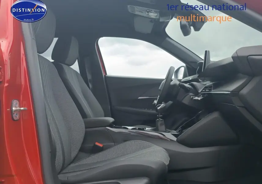Vue intérieure côté conducteur de la Peugeot 2008 rouge elixir, montrant sièges tissu et tableau de bord moderne.