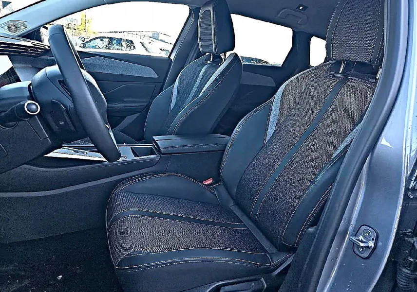Vue intérieure côté conducteur de la Peugeot 308 SW 2025 gris Artense, avec sièges tissu et accoudoir central.