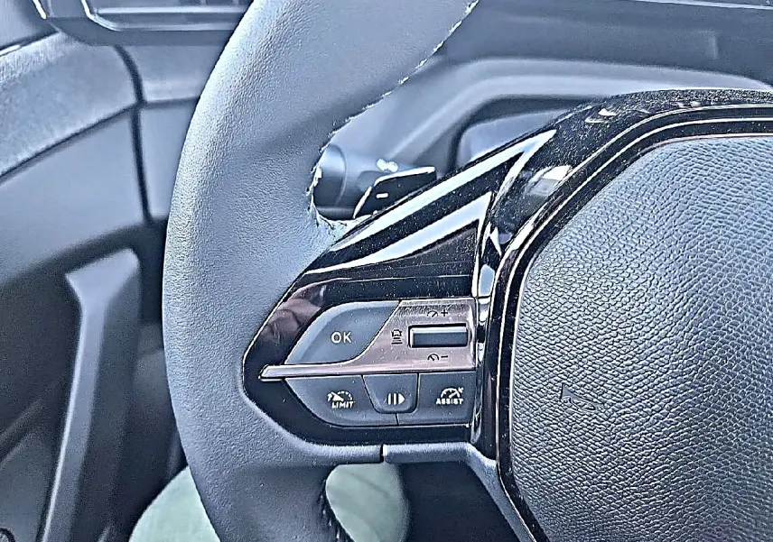 Gros plan sur le côté gauche du volant noir de la Peugeot 308 SW 2025 avec commandes multifonctions intégrées.
