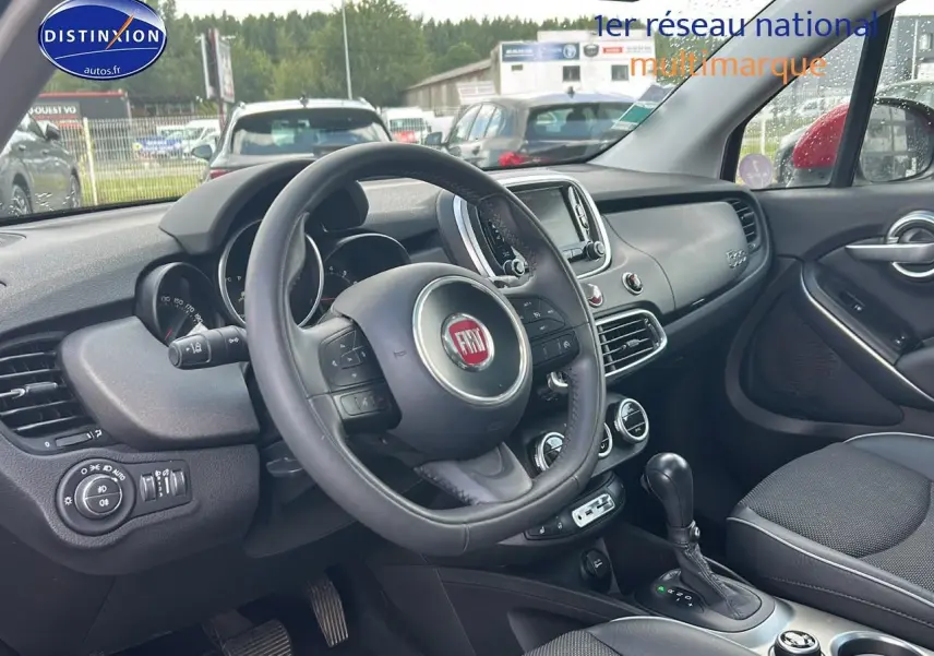 Intérieur de la Fiat 500X rouge, vue côté conducteur, volant cuir multifonction et tableau de bord moderne.