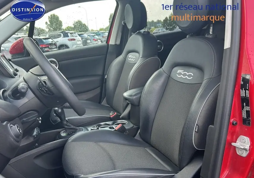 Vue intérieure côté conducteur d'une FIAT 500X rouge, sièges noirs avec logo 500 brodé sur les appuie-têtes.