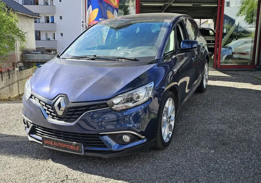 Renault Scénic bleu cosmos métal vu de 3/4 avant droit, avec calandre et phares modernes visibles.
