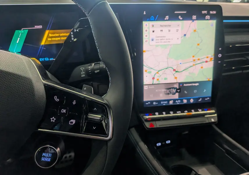 Intérieur du Renault Austral hybride 2025, vue du volant avec commandes tactiles et écran central tactile affichant la navigation.