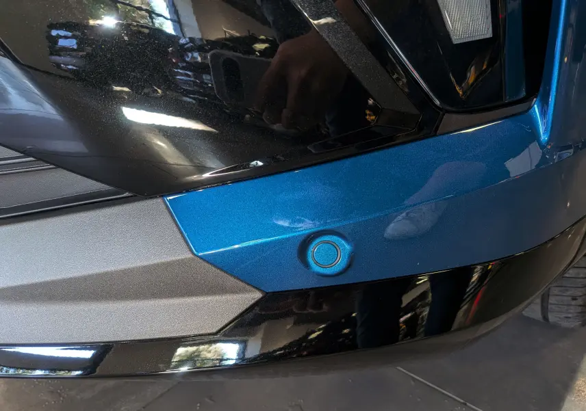 Gros plan sur le capteur de stationnement arrière intégré dans le pare-chocs bleu outremer du Renault Austral 2025.