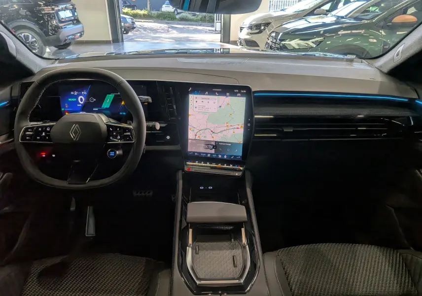 Intérieur du Renault Austral hybride 2025 vu de face, tableau de bord moderne avec écran tactile vertical et éclairage bleu.