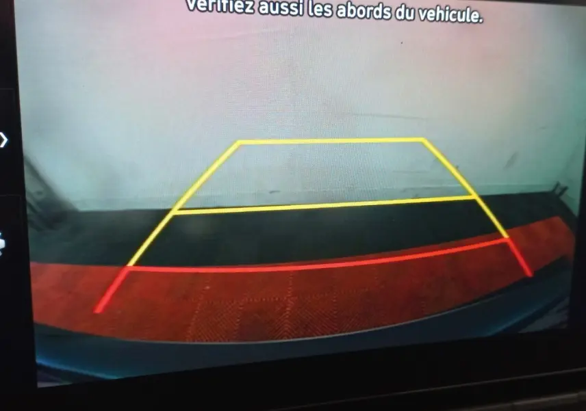 Vue caméra de recul du Hyundai Kona gris foncé, affichant les lignes de guidage jaune et rouge sur sol noir et rouge.