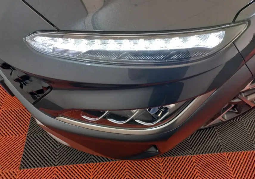 Gros plan sur le phare avant droit allumé d'une Hyundai Kona 1.6 Hybrid gris foncé, avec détails LED et calandre noire.
