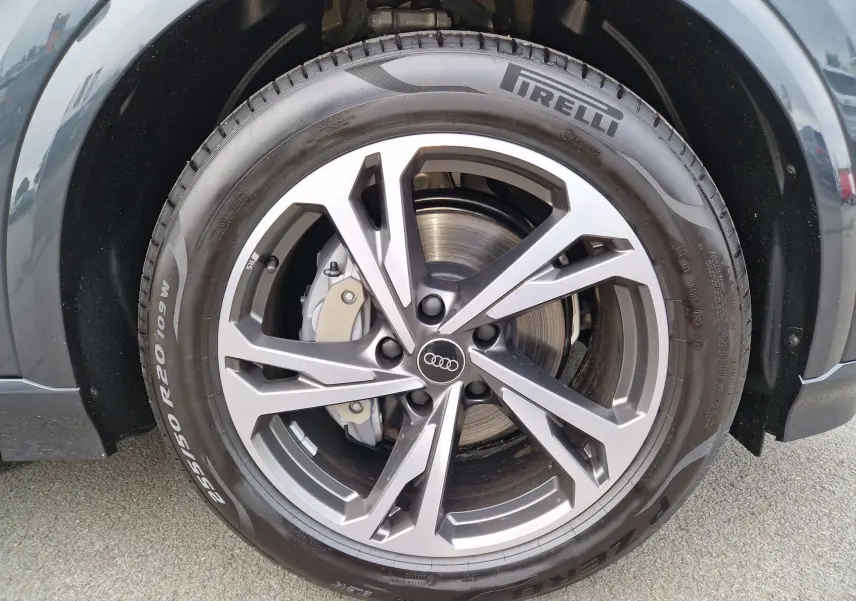 Gros plan sur la jante alliage grise et le pneu Pirelli du côté avant droit de l'Audi Q6 e-tron Performance S-Line gris Manhattan.