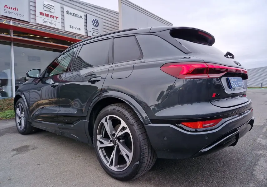 Vue 3/4 arrière droite d’un Audi Q6 e-tron Performance S-Line gris Manhattan avec jantes sport et feux LED distinctifs.