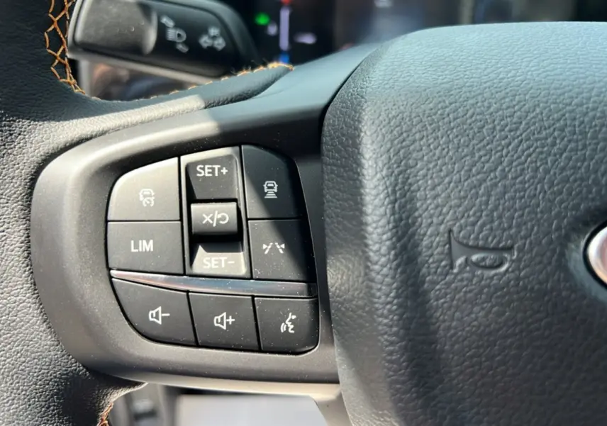 Gros plan sur les commandes au volant en cuir noir du Ford Ranger Wildtrak 2025, boutons multifonctions visibles.
