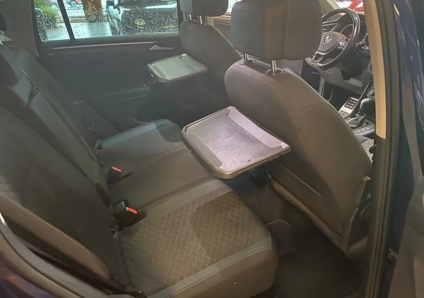 Vue intérieure arrière du Volkswagen Tiguan bleu vert 2020, sièges noirs avec tablettes pliantes intégrées aux dossiers avant.