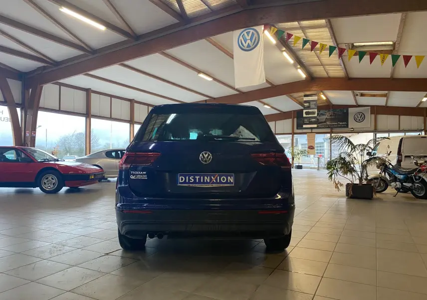 Vue arrière d'un Volkswagen Tiguan bleu vert 2020 dans un showroom avec drapeau VW suspendu au plafond.