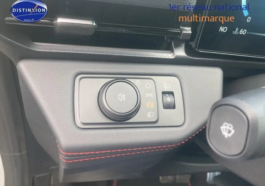 Gros plan sur le bouton de réglage des phares avec surpiqûres rouges sur le tableau de bord du Ford Puma gris cactus 2025.