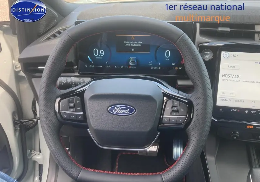 Vue rapprochée du volant perforé avec surpiqûres rouges et tableau de bord numérique du Ford Puma gris cactus 2025.