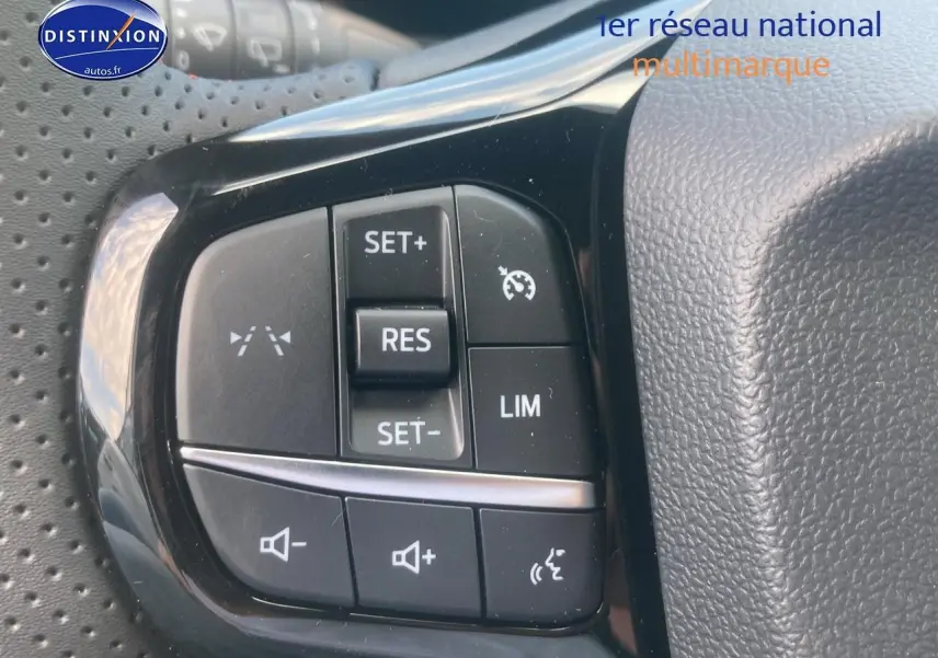 Gros plan sur les commandes du régulateur de vitesse et volume au volant d'une Ford Puma gris cactus 2025.