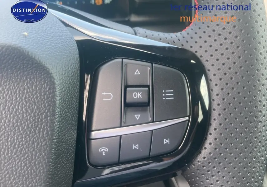 Gros plan sur les commandes multifonctions noires du volant perforé d'un Ford Puma gris cactus 2025.